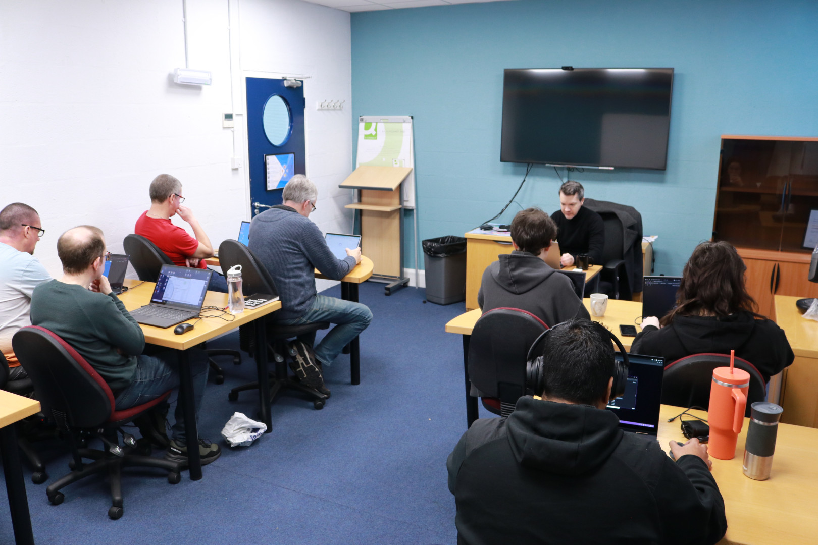 the technical team at Dolphin, sitting in rows of desks with their laptops, face the front of the room where James is talking to them